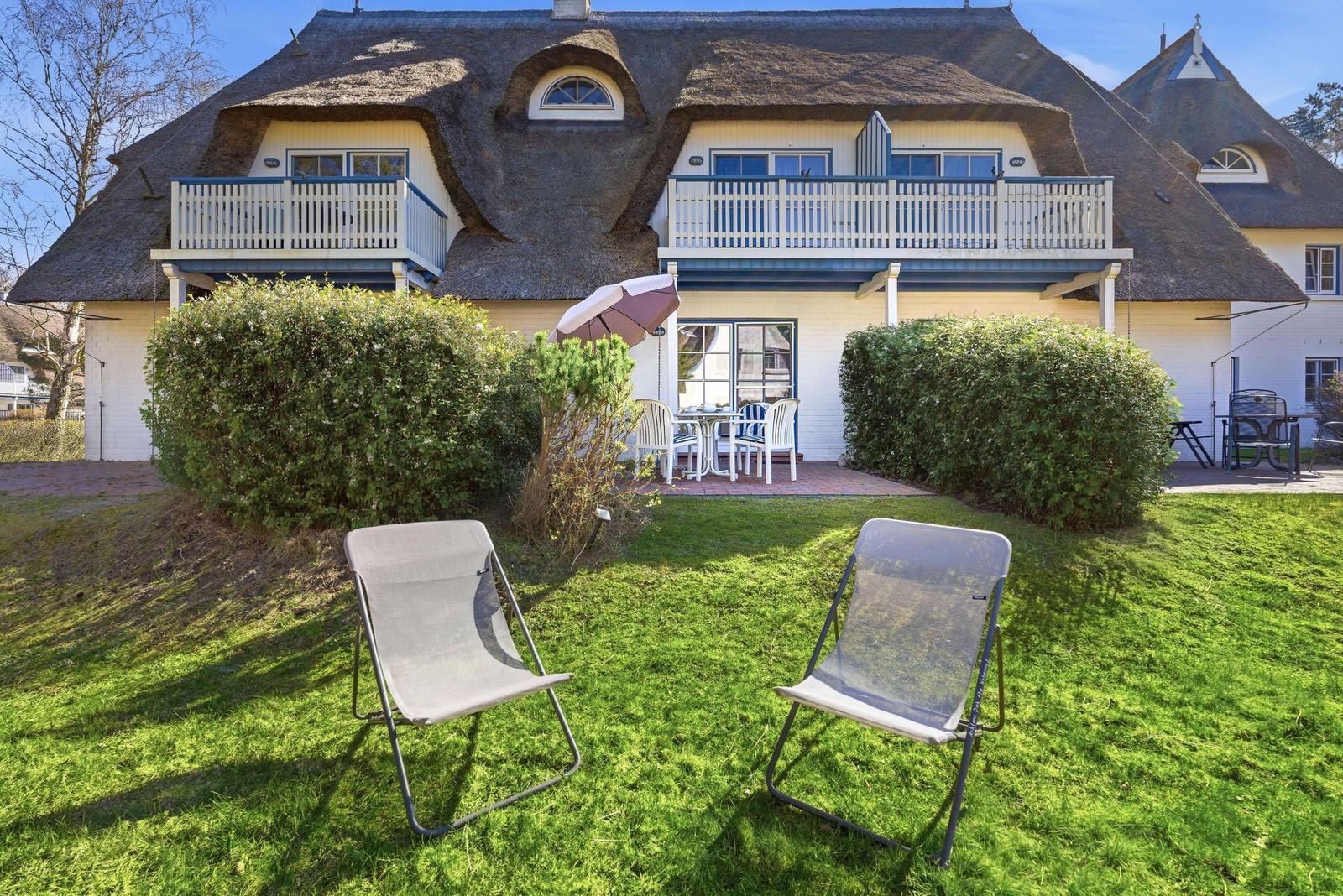 Haus mit Strohdach, Terrasse und Garten mit Liegestühlen.