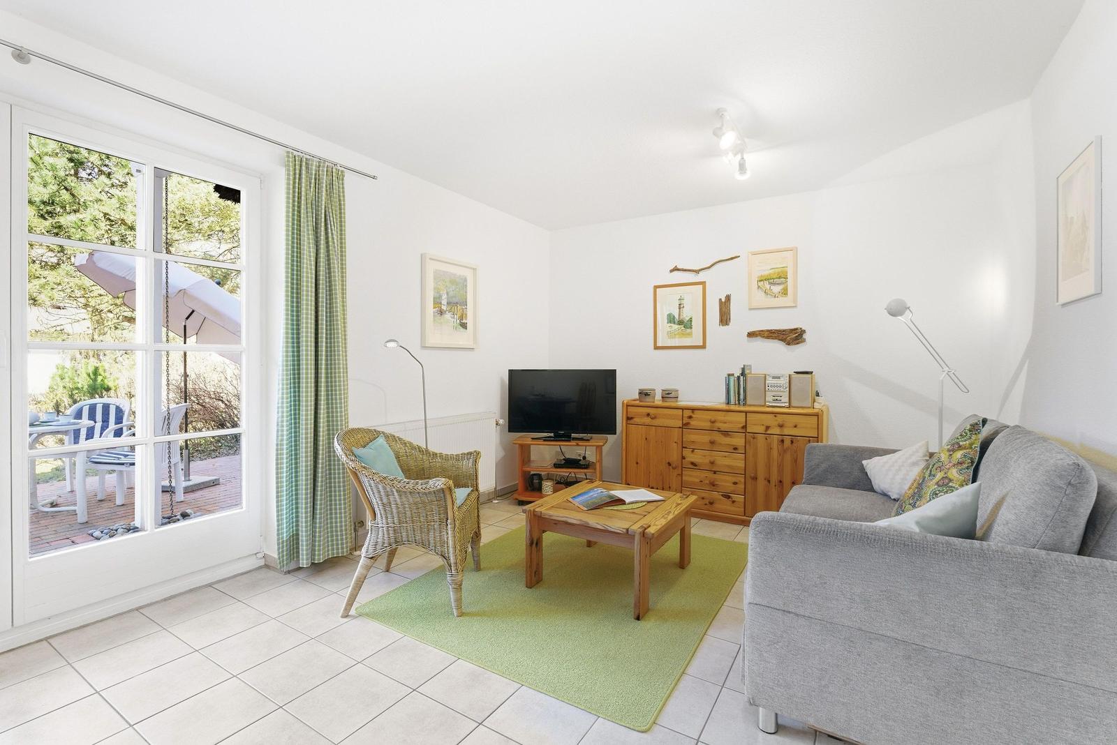 Wohnzimmer mit Sofa, Sessel, Fernseher und Terrasse.