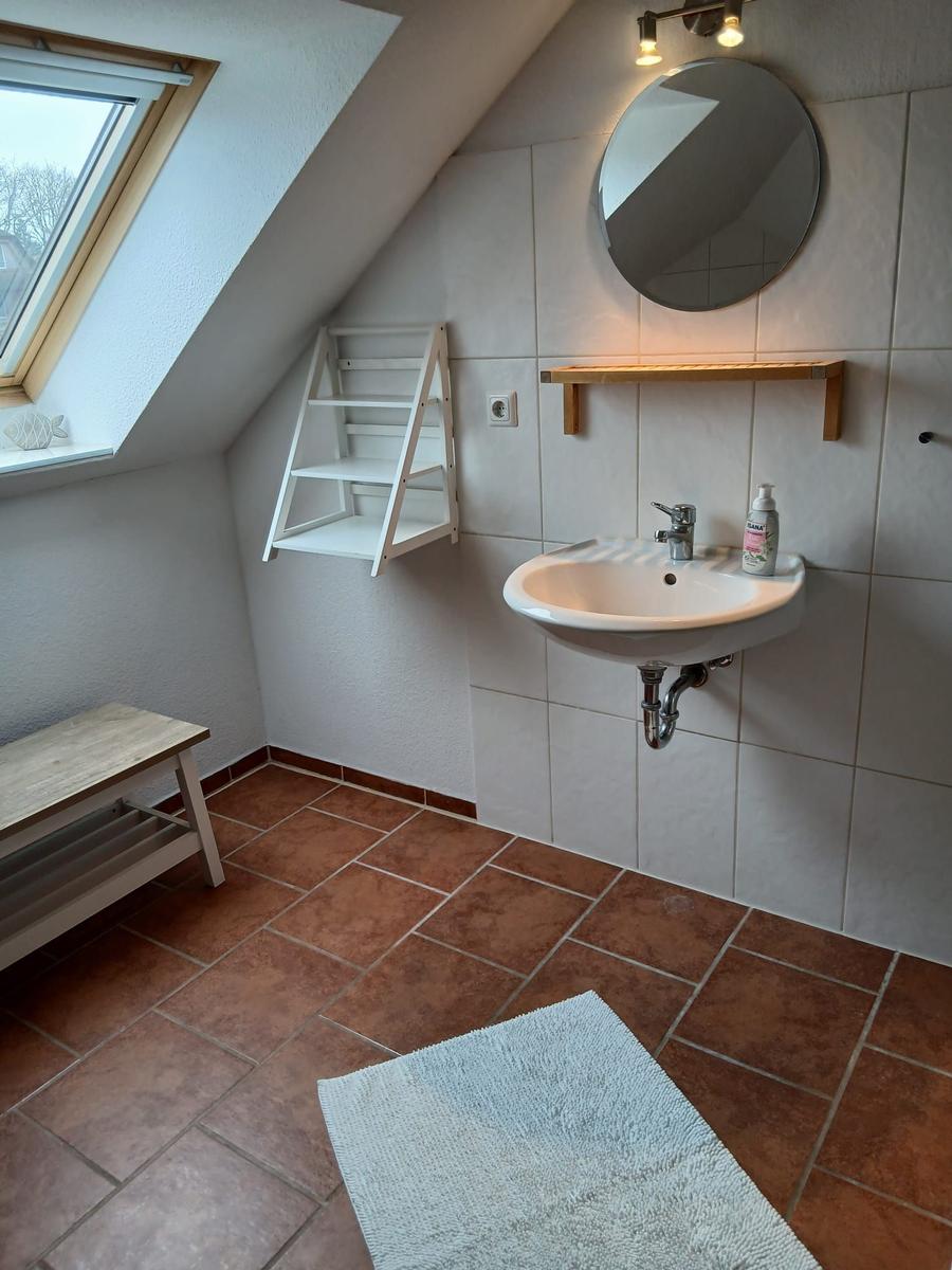 Badezimmer mit Waschbecken, Spiegel, Dachfenster und Holzregal an der Wand.