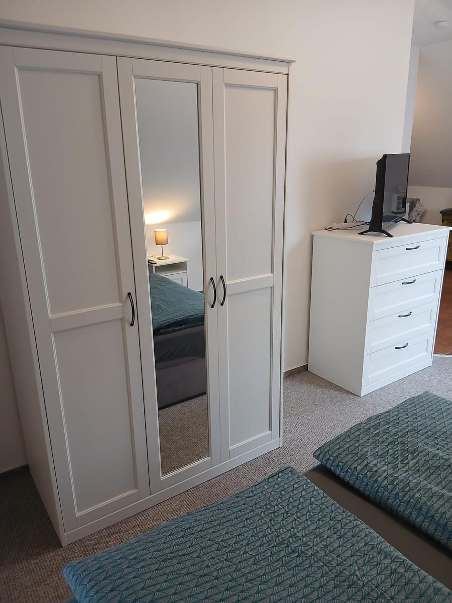 Schlafzimmer mit Kleiderschrank, Schrank mit Spiegeltüren und Fernsehgerät auf Kommode.