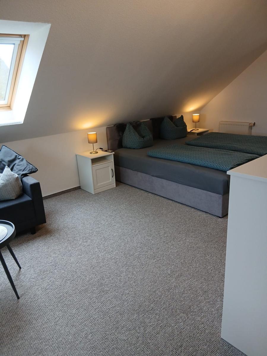 Schlafzimmer mit Doppelbett, Nachttisch und Sessel unter Dachschrägen.