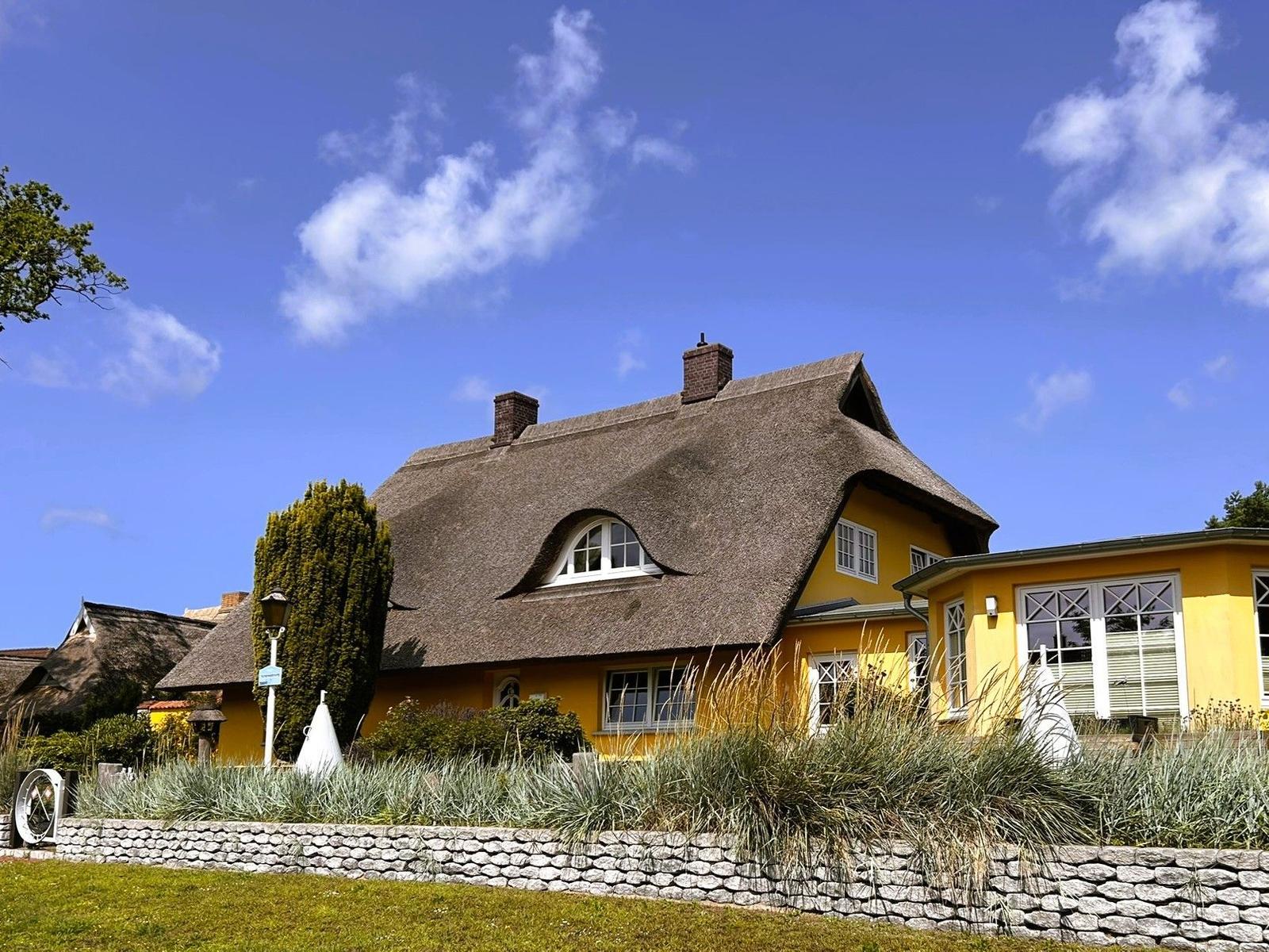 Gelbes Haus mit strohgedecktem Dach und Steinmauer im Vorgarten.