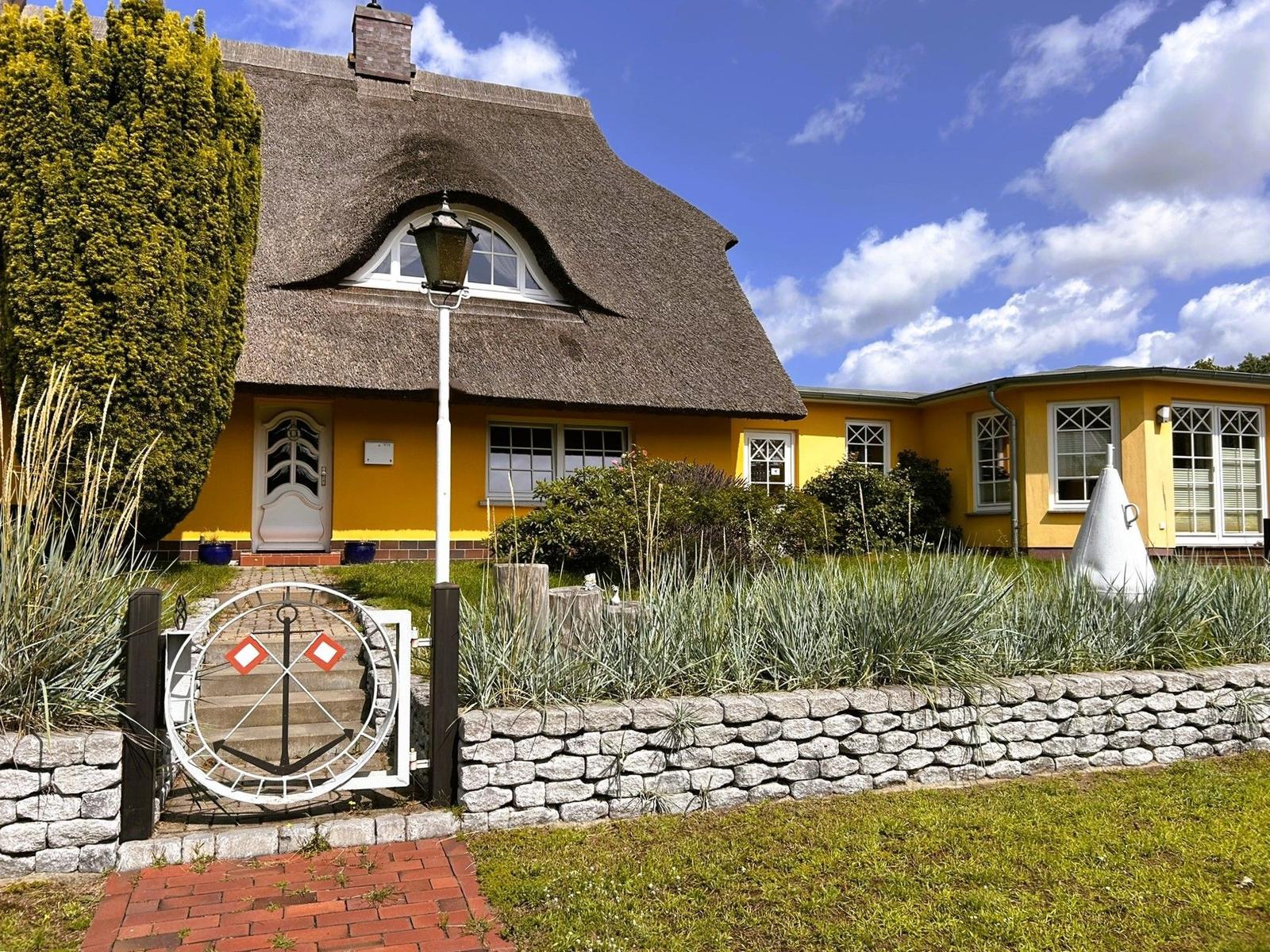Ein gelbes Haus mit strohgedecktem Dach und Gartenzaun.