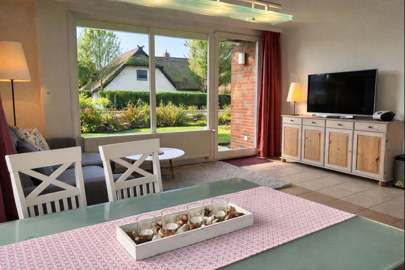 Wohn- und Essbereich mit Blick auf Garten und Haus. Tisch, Stühle, Fernseher und TV-Schrank.