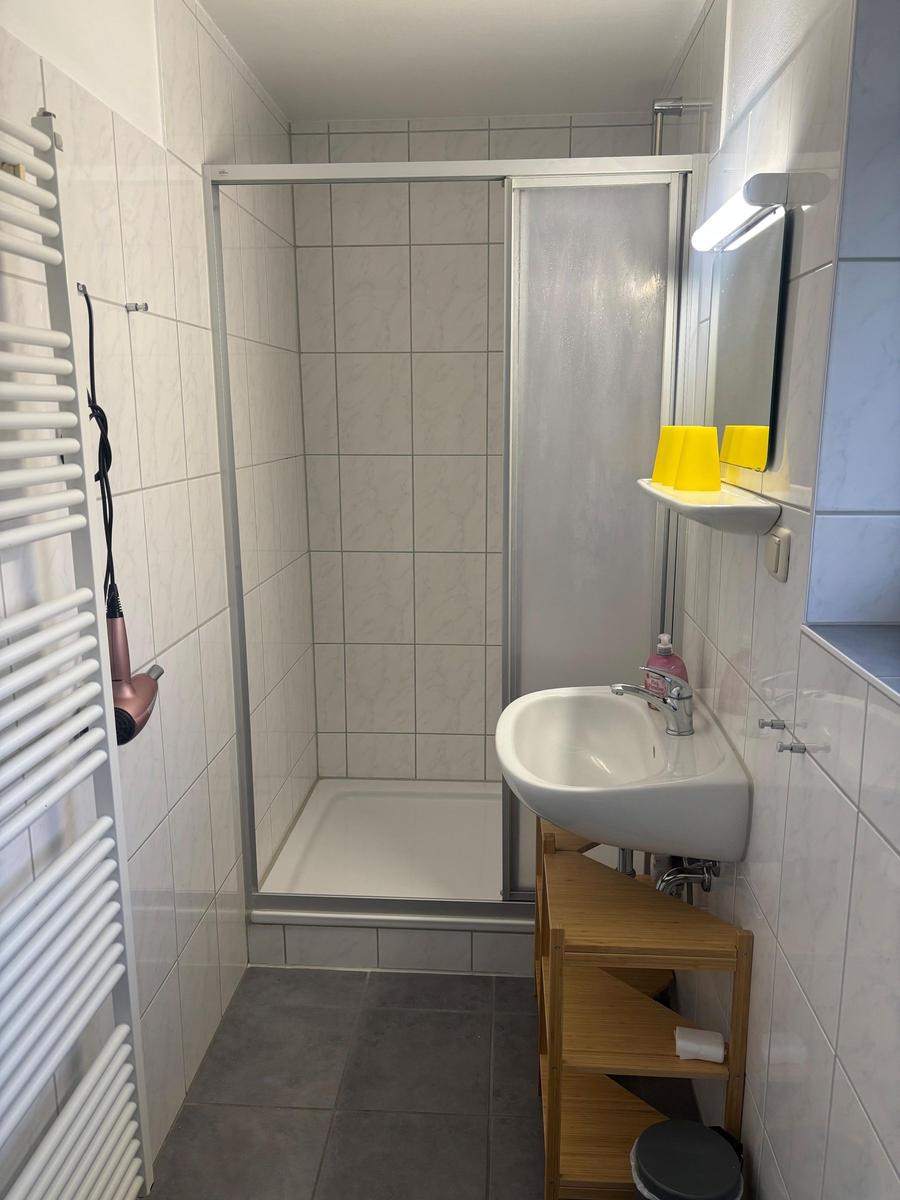 Badezimmer mit Dusche, Waschbecken und Heizung. Gelbe Tassen auf dem Regal.