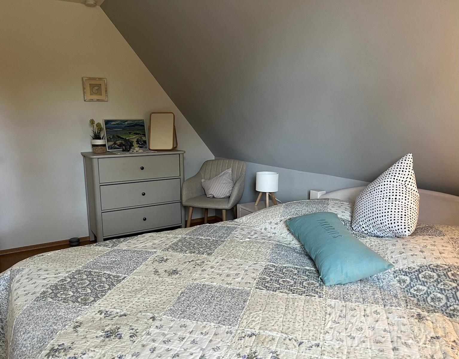 Schlafzimmer mit Dachschrägen, Bett mit gemustertem Bettbezug und Nachttisch.