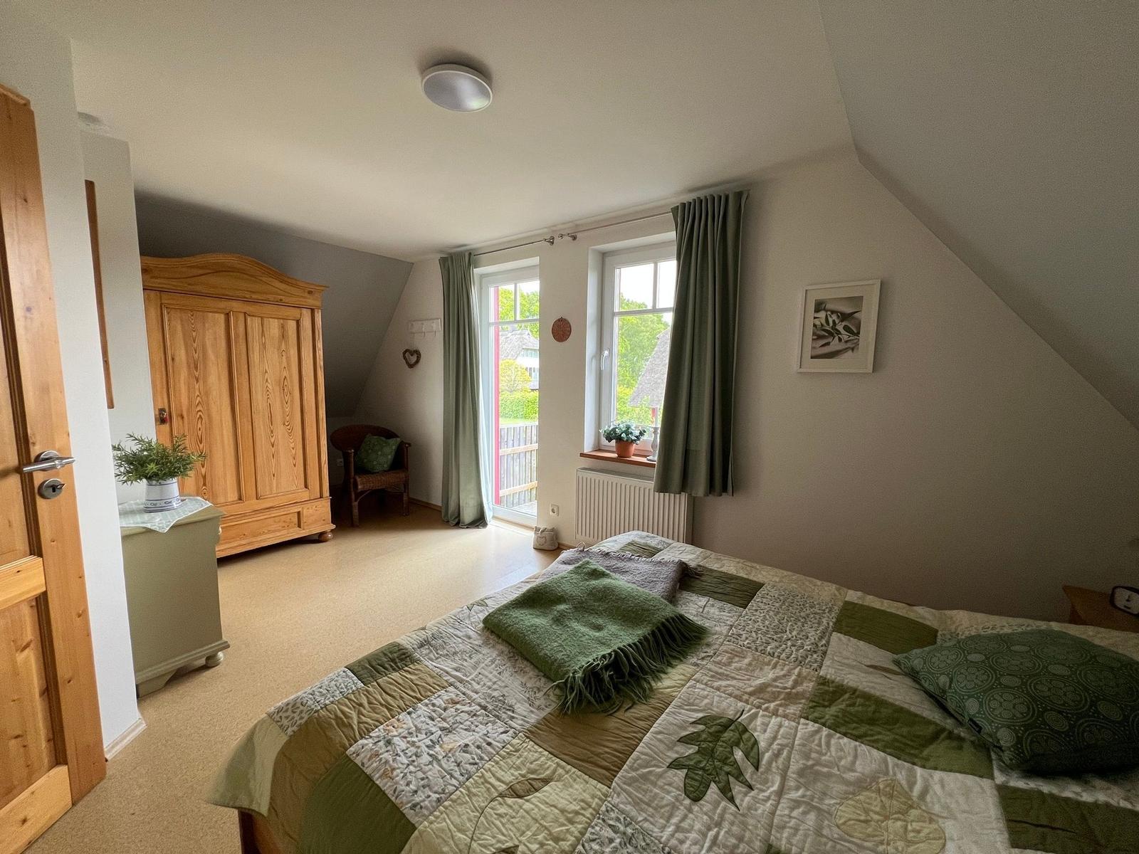 Schlafzimmer mit Bett, Kleiderschrank und Fenster zur Terrasse.