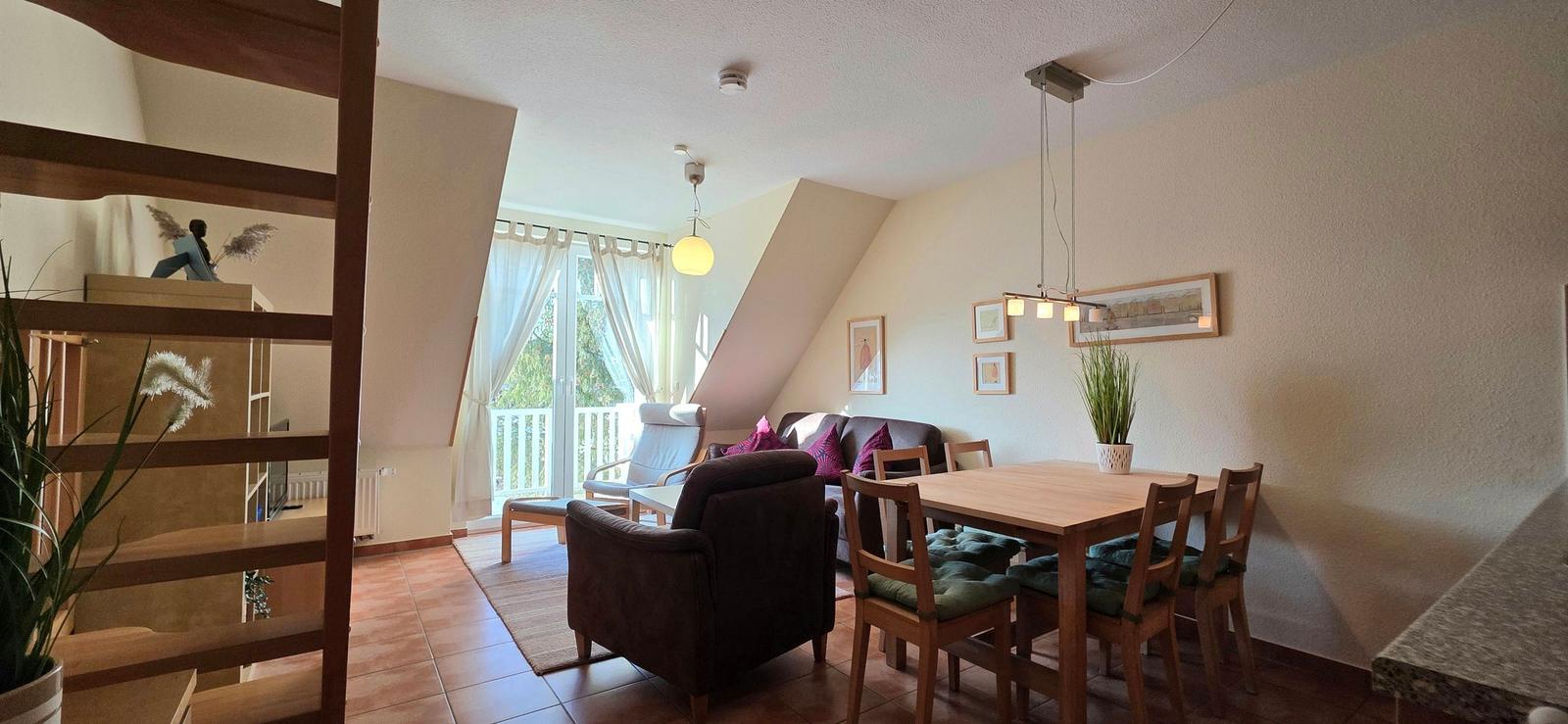 Wohn- und Essbereich mit Holztisch, Stühlen und Sofa unter Dachschrägen.