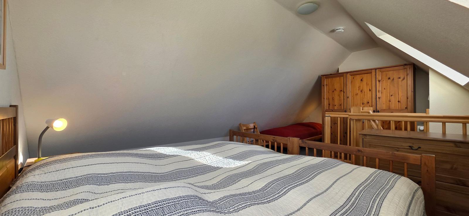 Schlafzimmer mit Dachschrägen, Bett, Kleiderschrank und Fenster