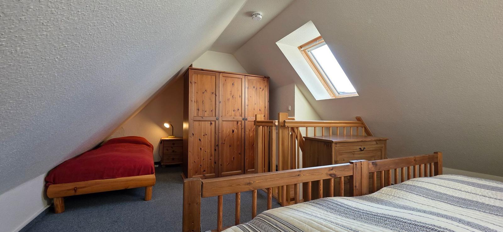 Zimmer mit zwei Betten, Holzmöbel und Dachschräge mit Dachfenster.
