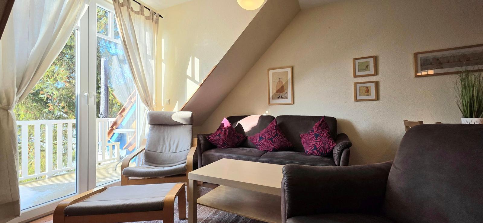 Wohnzimmer mit Sofa, Sessel und Glastür zum Balkon.