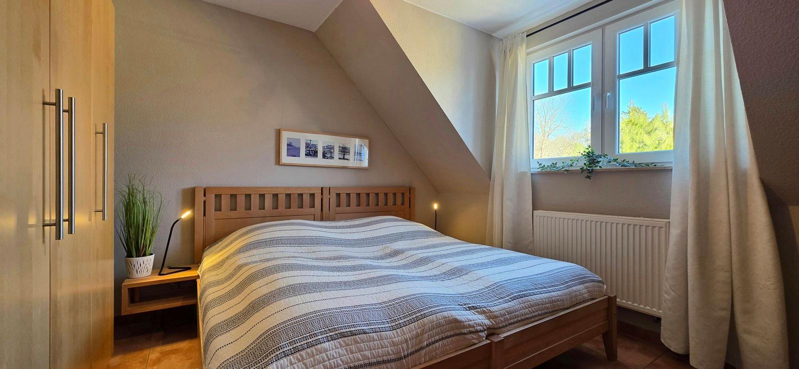 Schlafzimmer mit Dachschräge, Holzbett, Fenster und Gardinen.