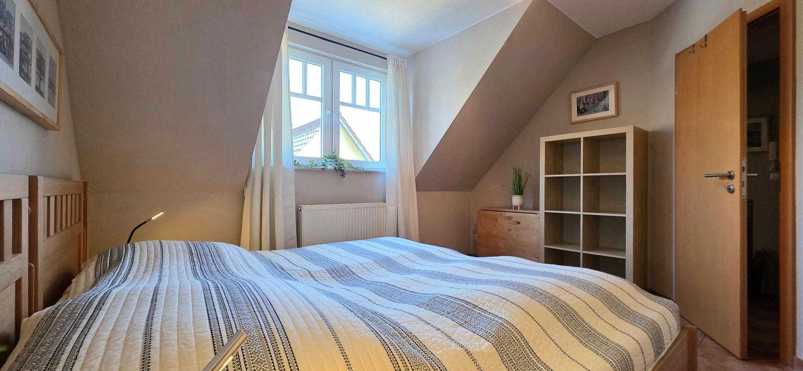 Schlafzimmer mit Dachschrägen, Bett, Schrank und Fenster mit Blick auf Dach.