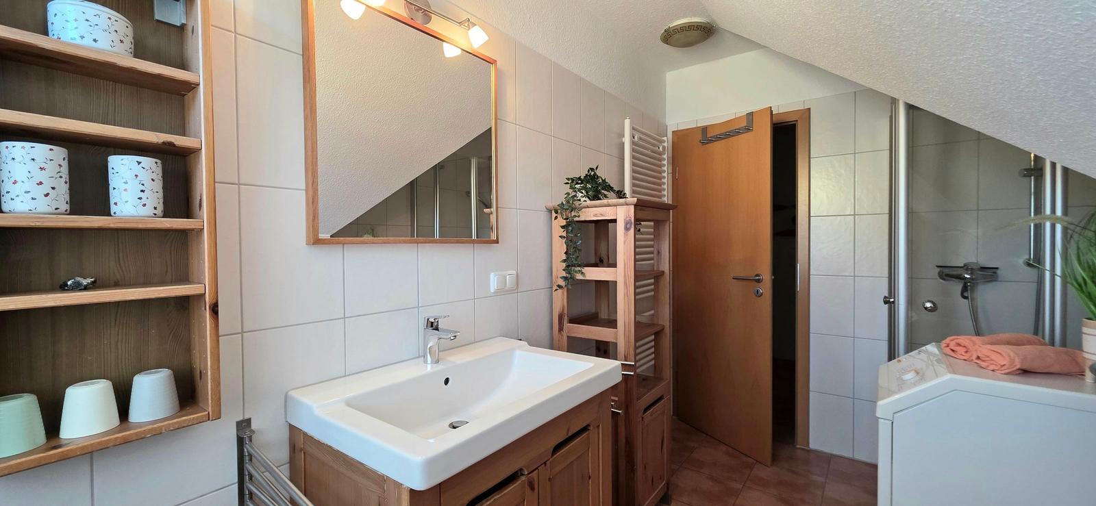 Badezimmer mit Waschbecken, Spiegel, Dusche und Holzregalen.