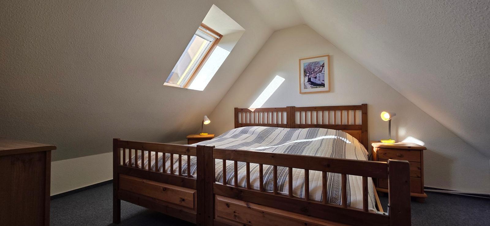 Schlafzimmer mit Dachschrägen, Holzbett, Nachttischen und Dachfenster.