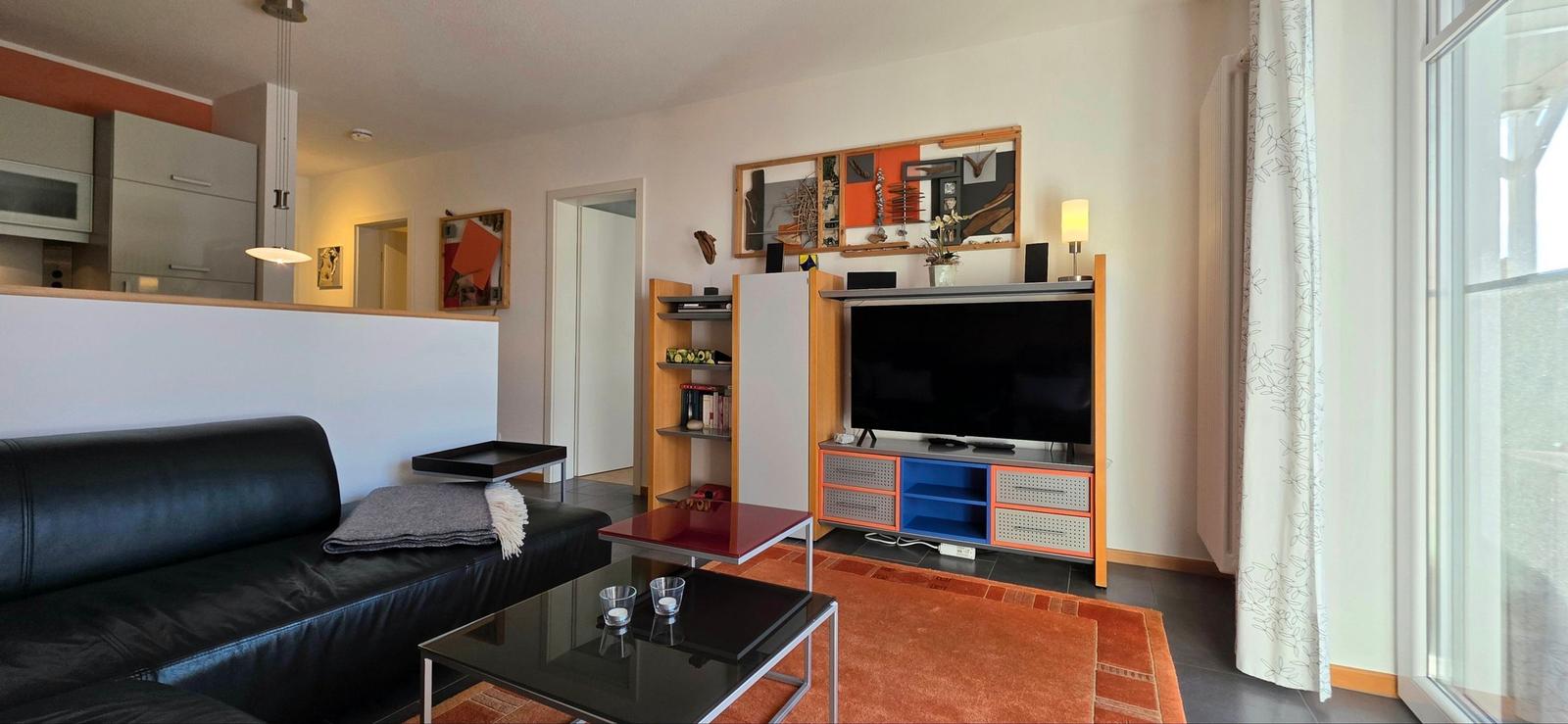 Wohnzimmer mit Sofa, Fernseher und Küchenbereich im Hintergrund.
