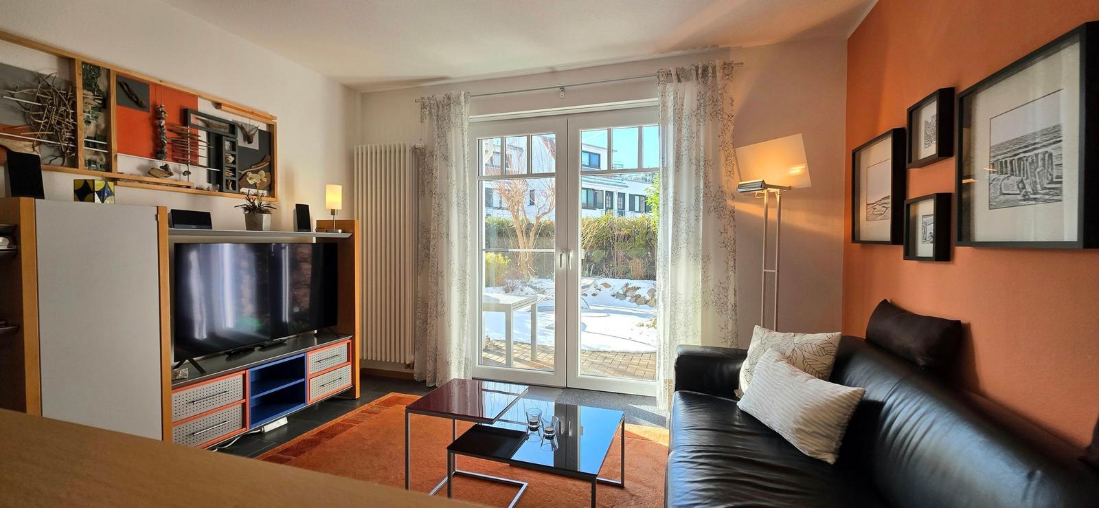 Wohnzimmer mit Sofa, Fernseher und Terrassentür. Wand mit Bildern und orange Wandfarbe.