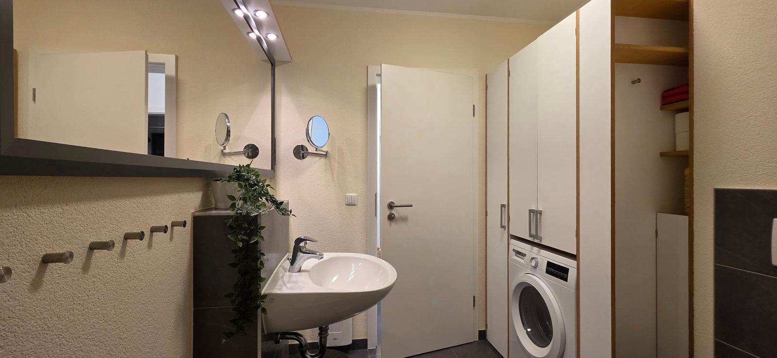 Badezimmer mit Waschmaschine, Spiegel und Pflanze