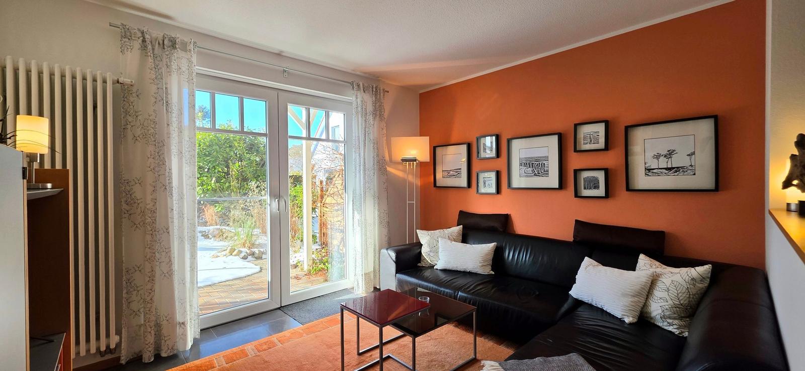 Wohnzimmer mit schwarzer Couch, orangefarbener Wand und Glas-Tür zum Garten.
