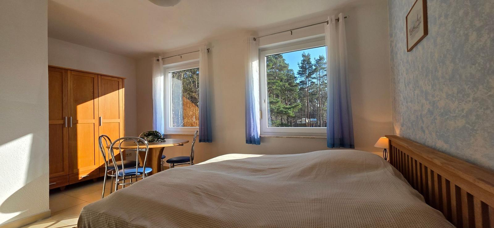 Schlafzimmer mit Bett, Schreibtisch und Fensterblick auf Wald.