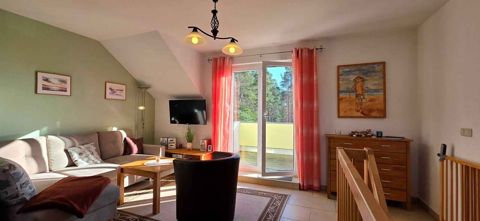 Wohnzimmer mit Sofa, Fernseher und Balkon. Rote Vorhänge und Holzmöbel.