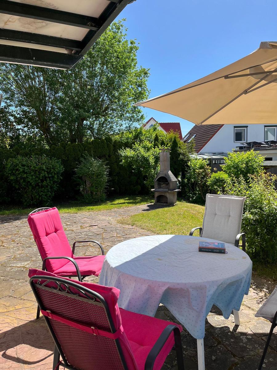 Runder Tisch mit Stühlen unter Sonnenschirm und Grill im Garten.
