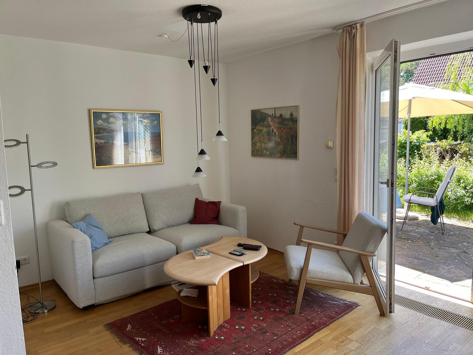 Wohnzimmer mit Sofa, Sessel, Tisch und Blick auf die Terrasse.