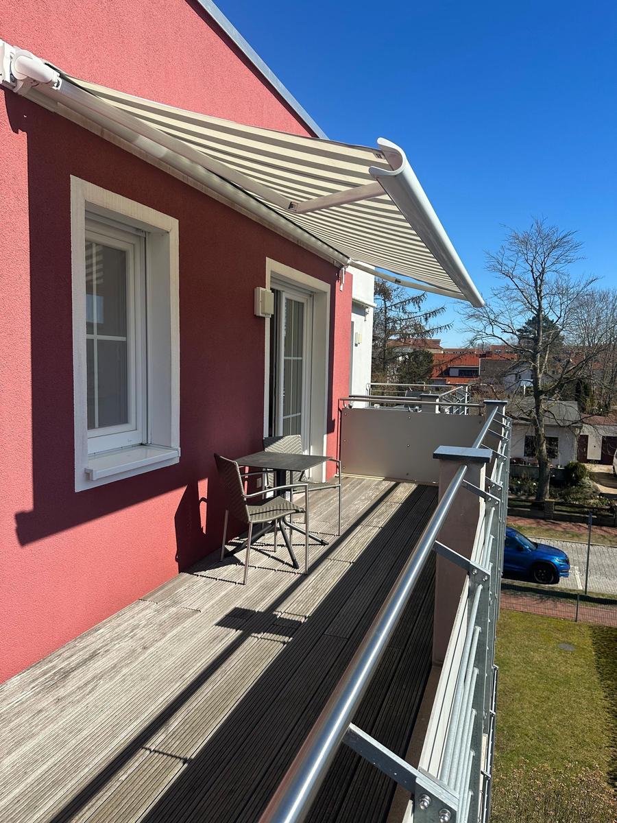 Terrasse mit Tisch und Stühlen, Sonnenschutz und Blick auf die Umgebung.