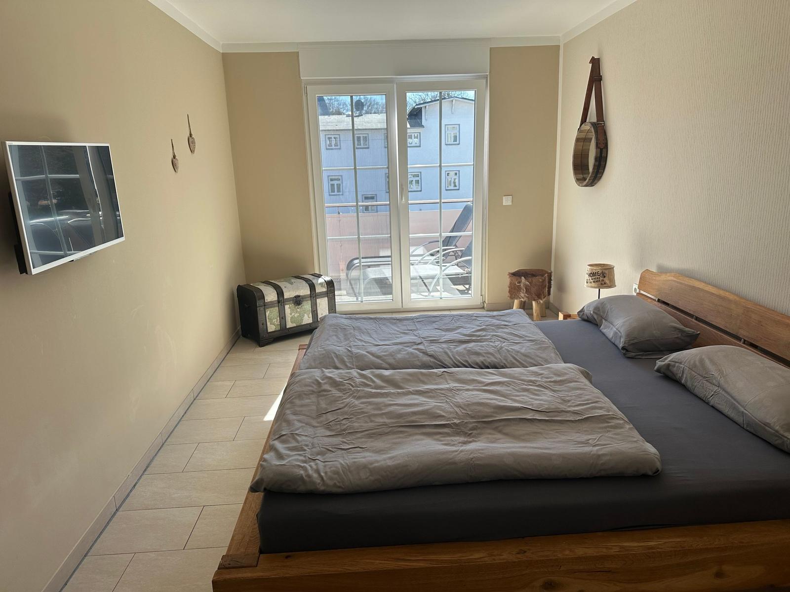 Schlafzimmer mit Doppelbett, Fernseher und Balkonansicht.