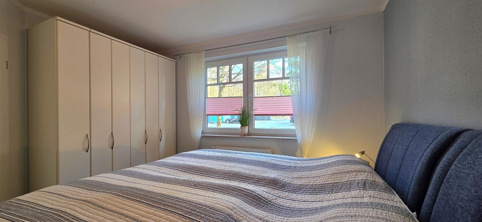 Bedroom with bed, wardrobe, and window with curtains.