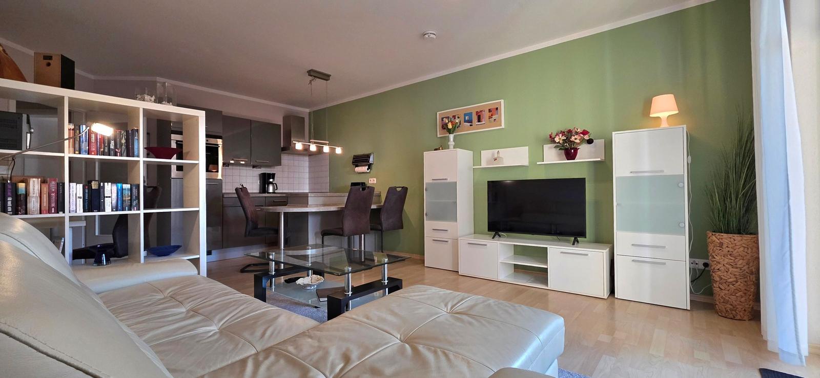 Living room with sofa, TV, and kitchen area in the background.