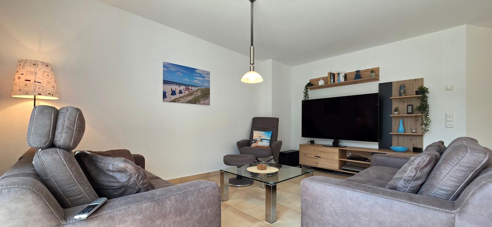 Wohnzimmer mit Sofa, Fernseher und Glas-Tisch.