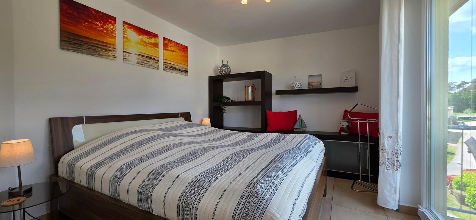 Schlafzimmer mit Doppelbett, Wandbildern und Fensterblick.
