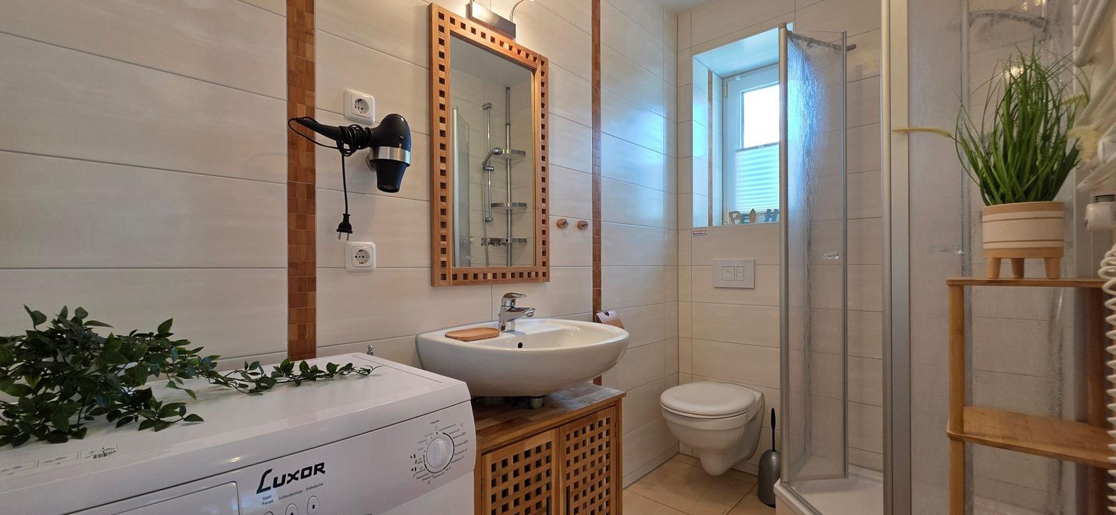 Badezimmer mit Waschmaschine, Spiegel, Dusche und Toilette.