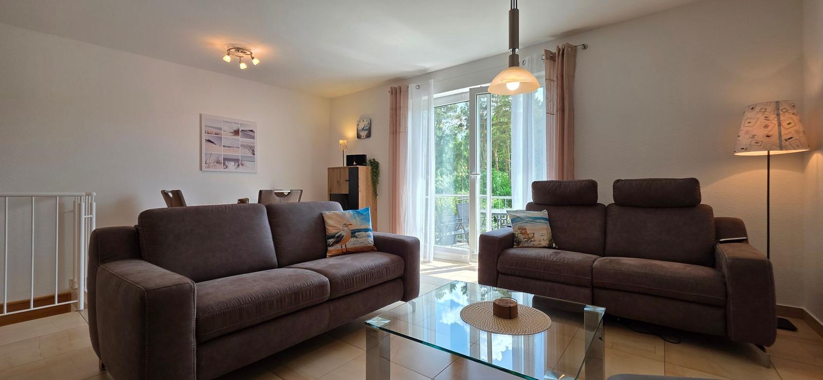 Wohnzimmer mit zwei braunen Sofas, Glas-Tisch und Balkontür.