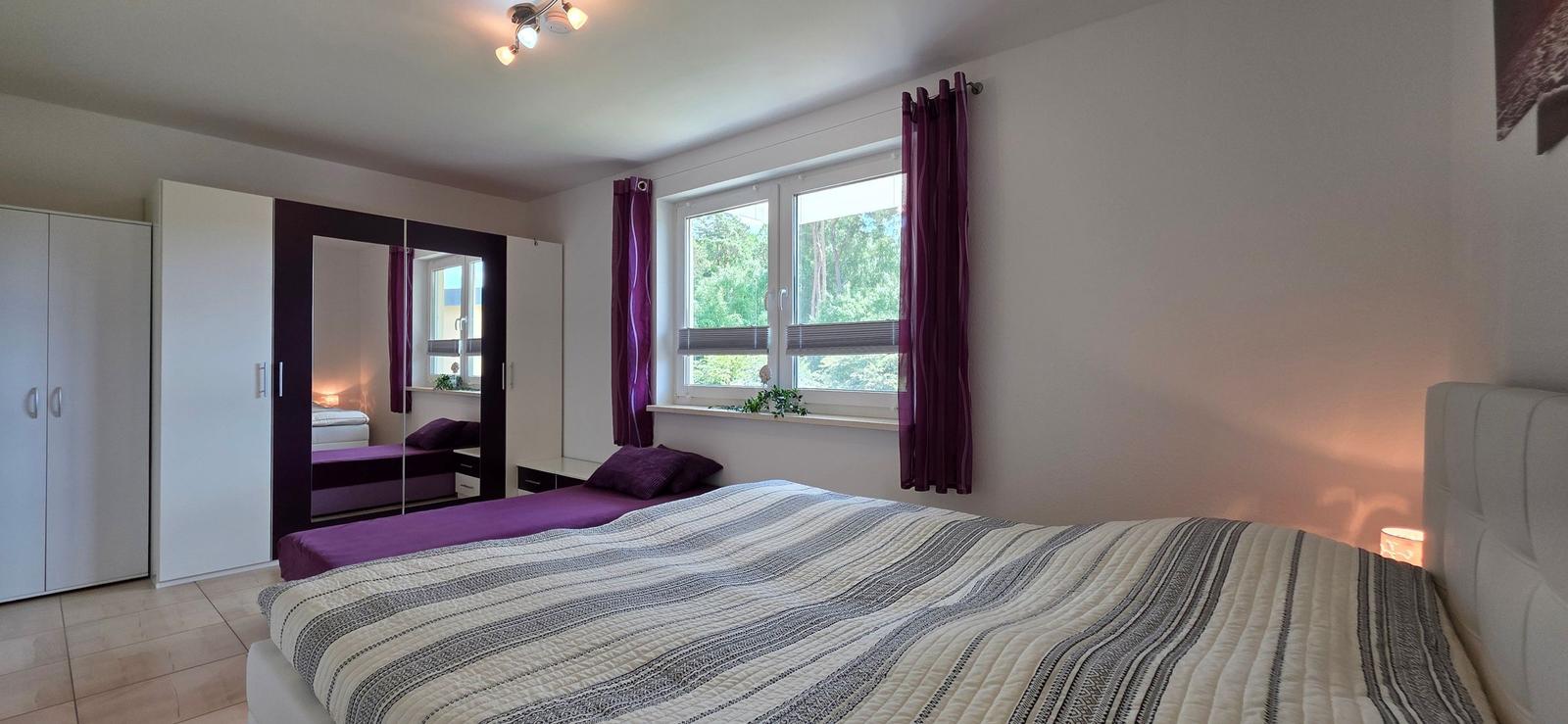Schlafzimmer mit Bett, Fenster, Gardinen und Kleiderschrank.