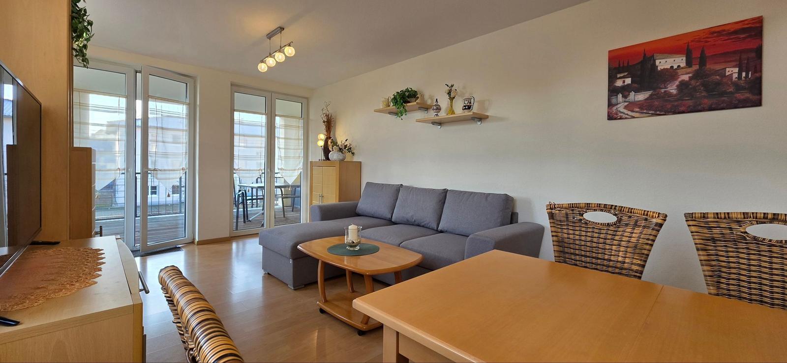 Wohnzimmer mit Sofa, Esstisch und Blick auf Balkon.