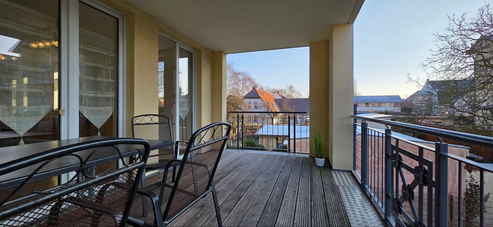 Terrasse mit Tisch und Stühlen, Blick auf Dächer und Bäume.
