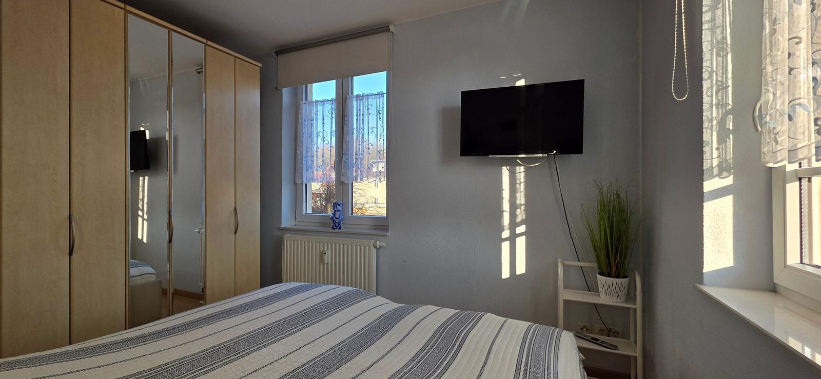 Schlafzimmer mit Bett, Kleiderschrank, TV und Fenster.