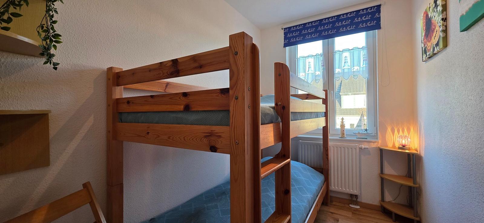 Zimmer mit Doppelstockbett, Fenster mit Vorhang und kleinem Nachttisch.