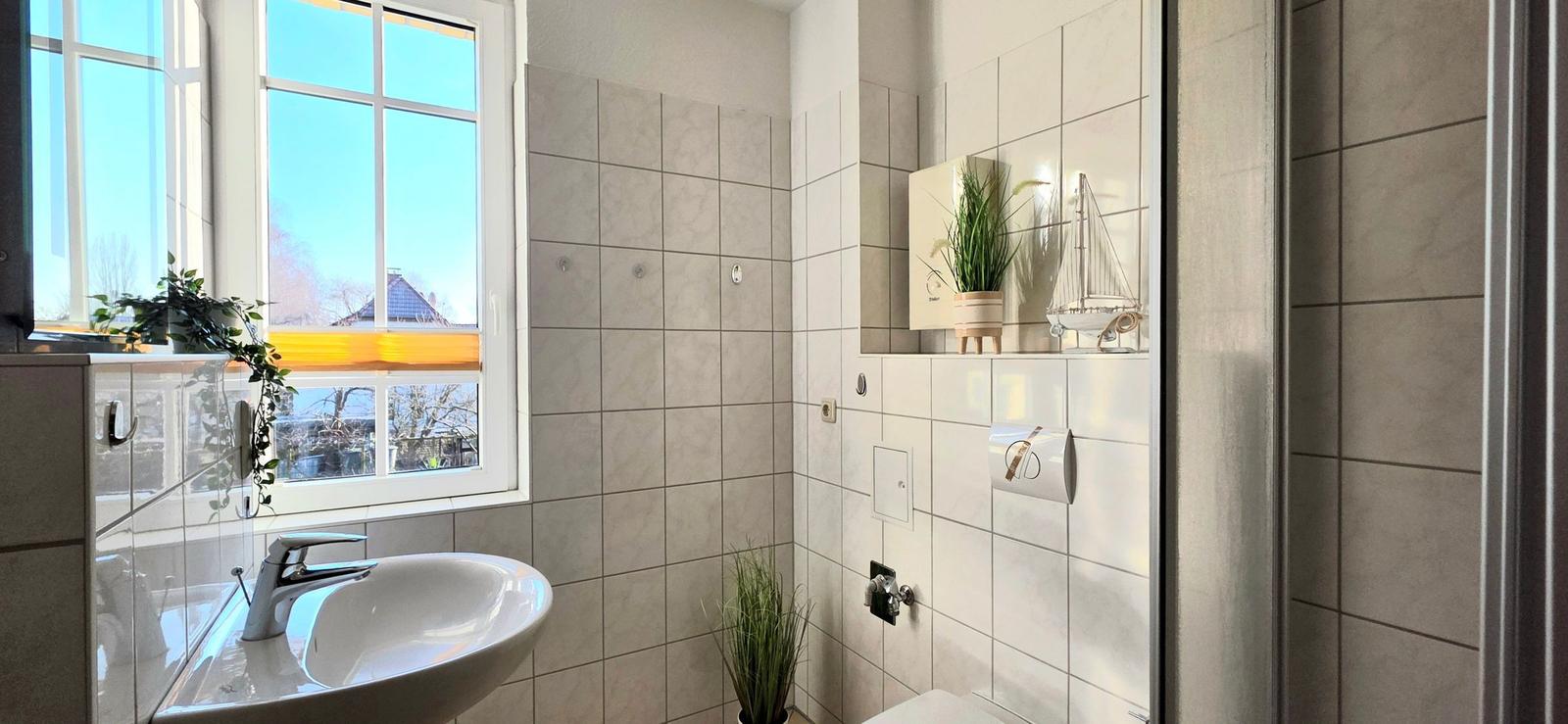 Badezimmer mit Waschbecken, Dusche und Fenster mit Blick auf Außenbereich.