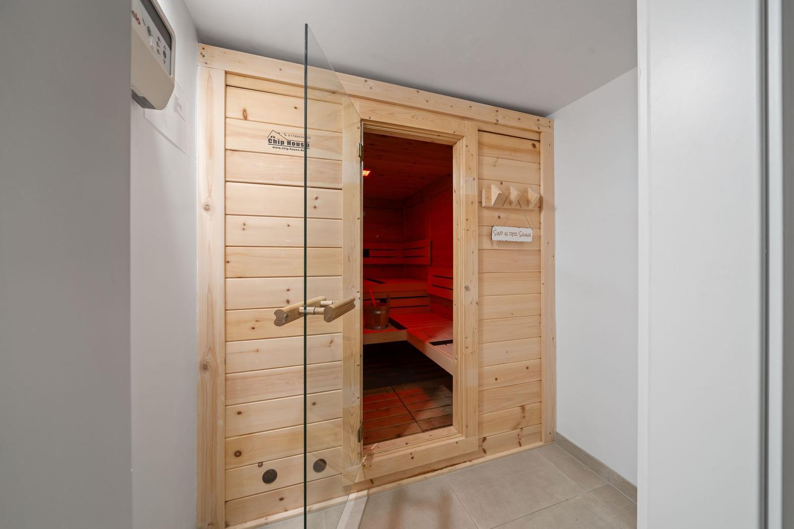 Sauna with wooden door and glass front. Interior benches and wooden floor visible.