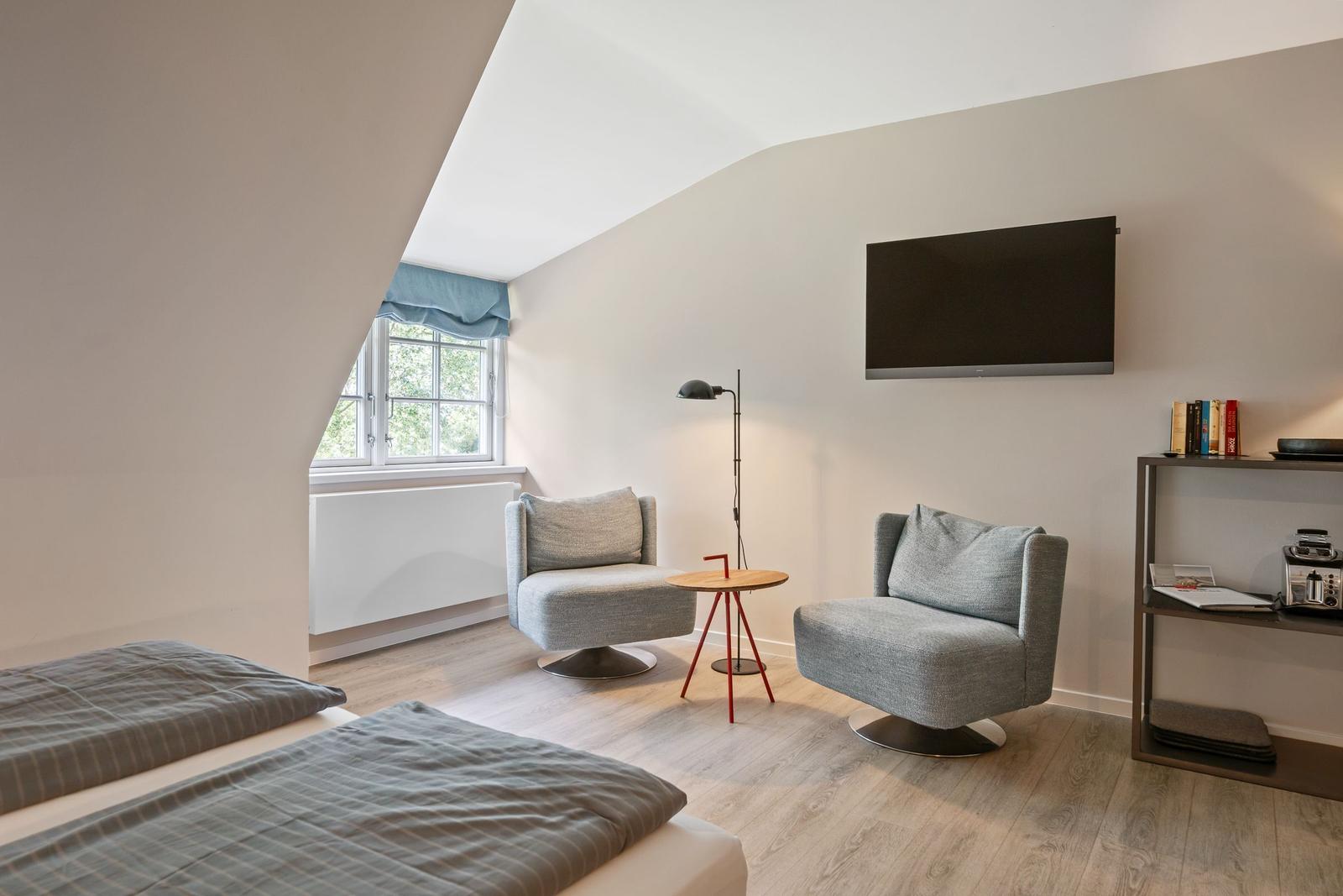 Room with double bed, two armchairs, TV, and window with view.