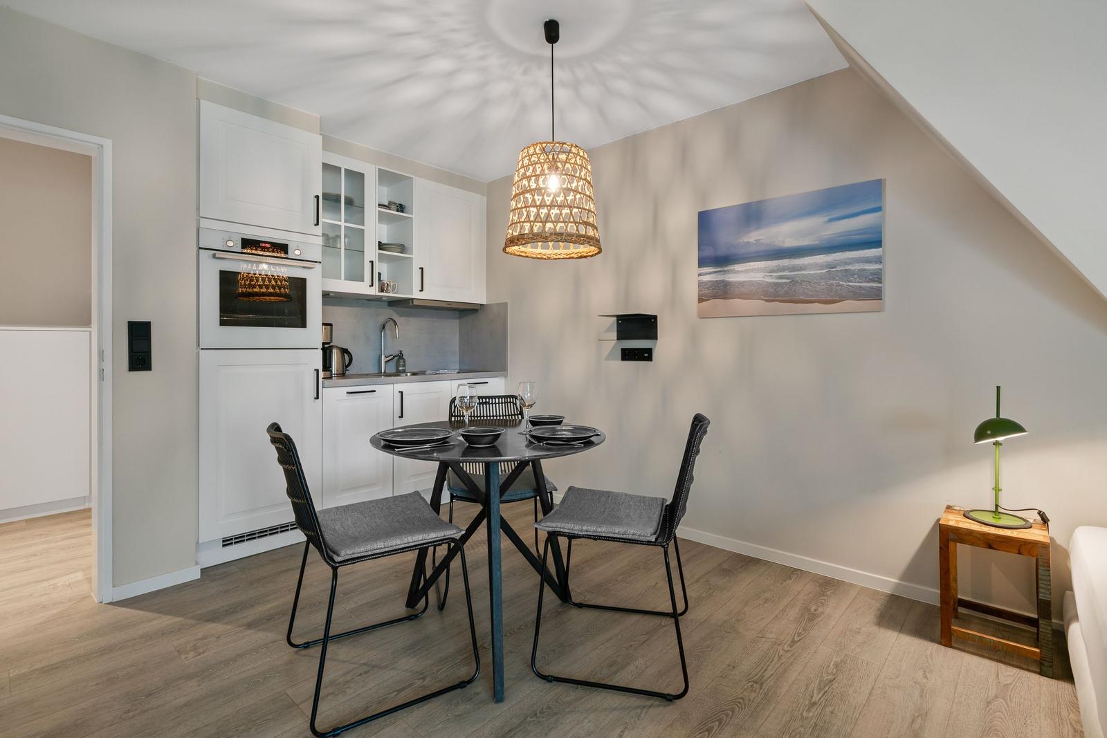 Kitchen with dining table, white cabinets, and pendant light under sloped ceiling.