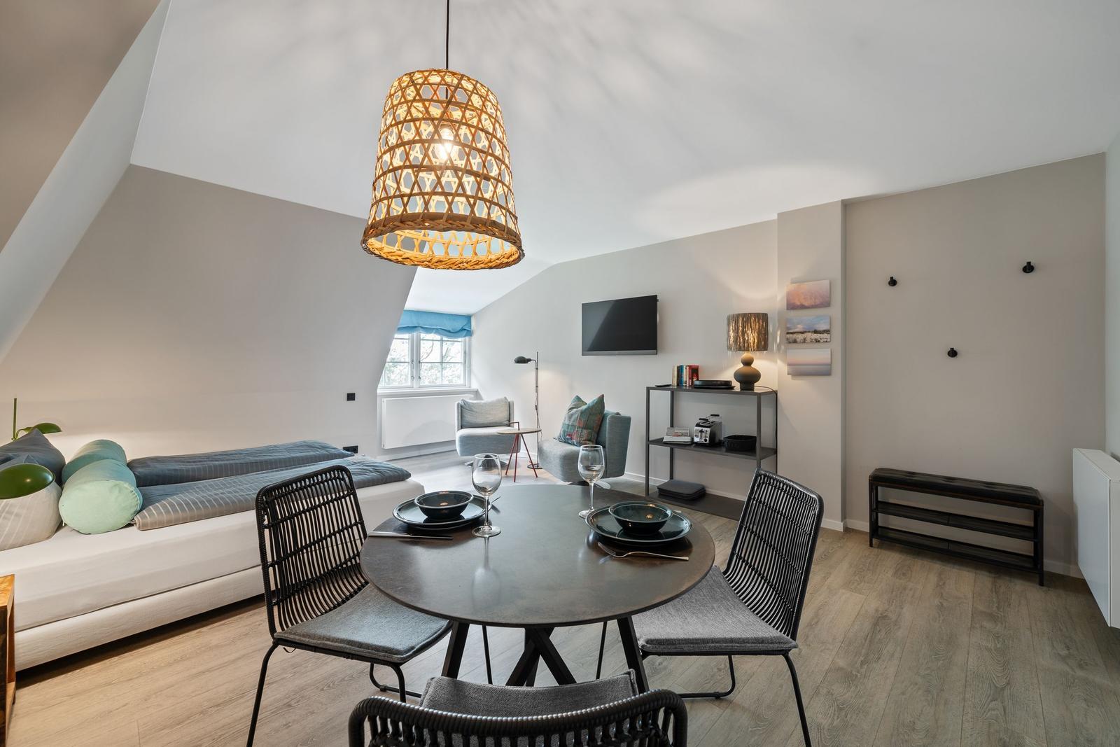 A room with dining area, sleeping space, and TV under a sloped ceiling.