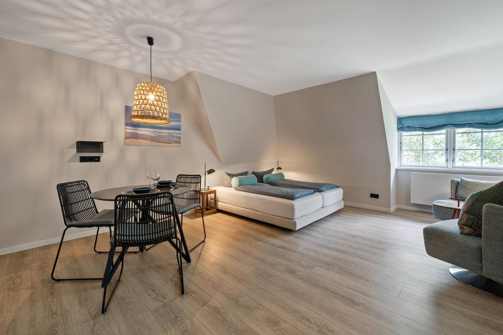 Bedroom with dining area and window. Wooden floor, bed, table, chairs, and sofa.