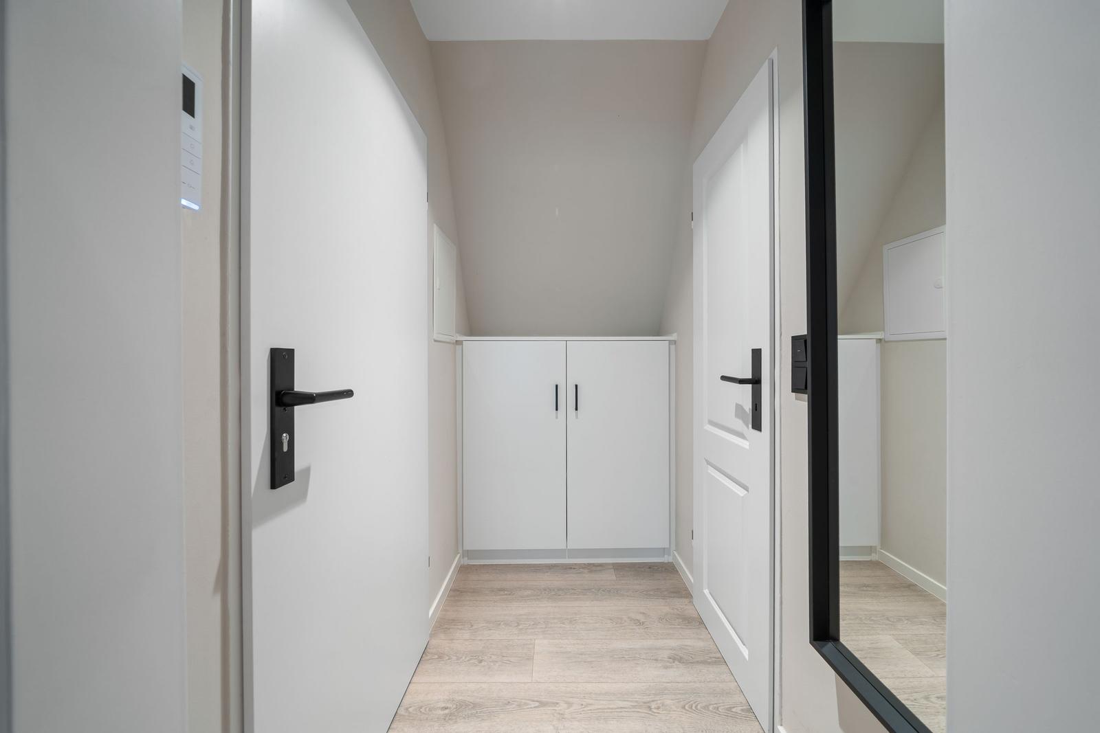 Hallway with white doors, cabinet, and wooden floor