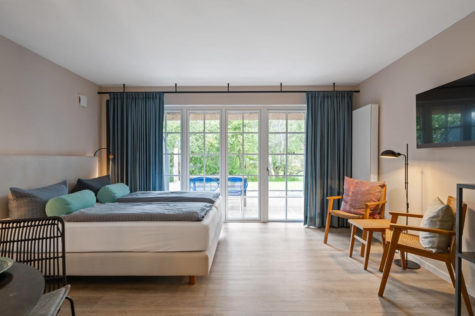 Schlafzimmer mit Doppelbett, Sitzgelegenheiten und Blick auf Garten.