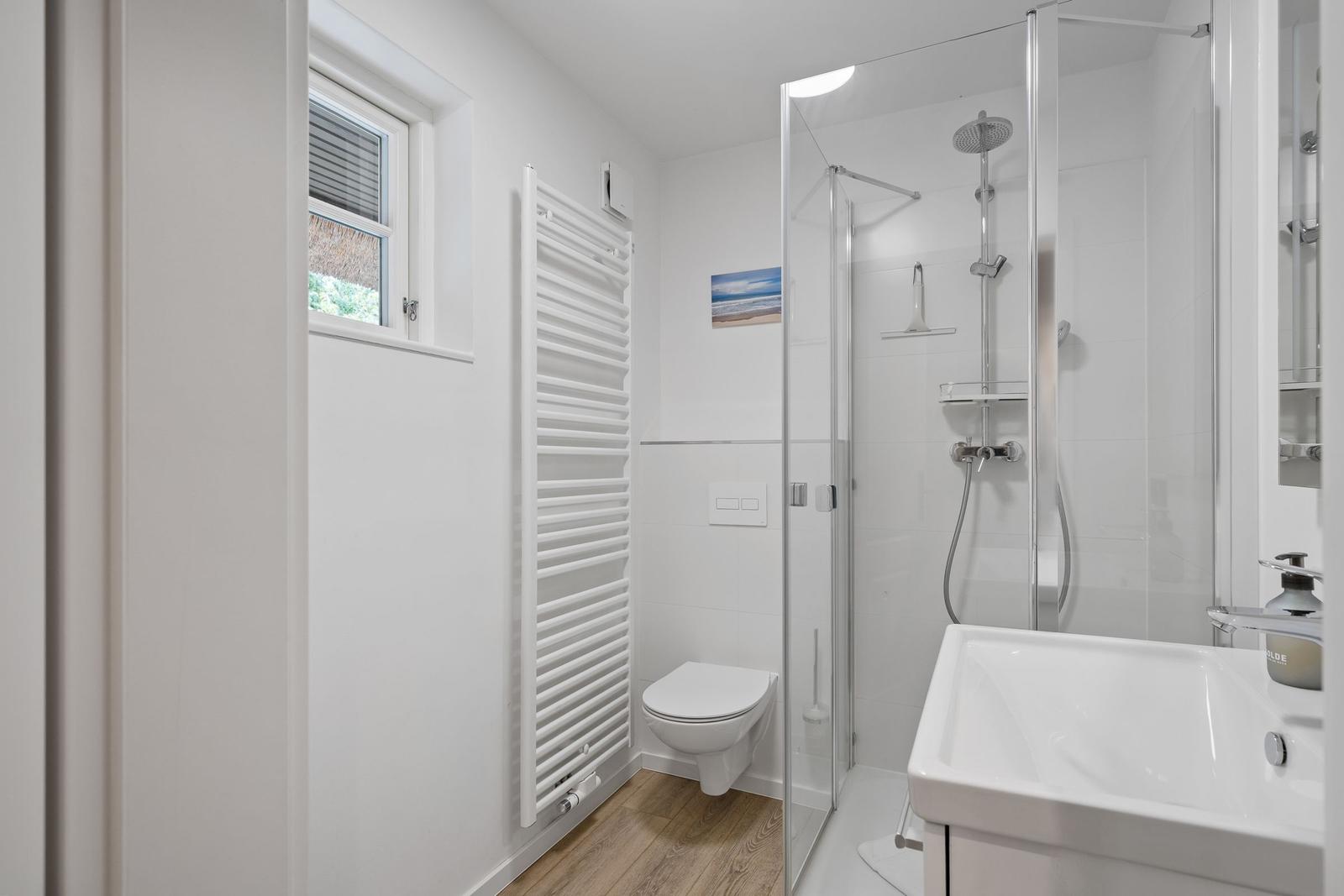 Badezimmer mit Dusche, Waschbecken und Toilette. Fenster mit Jalousie.