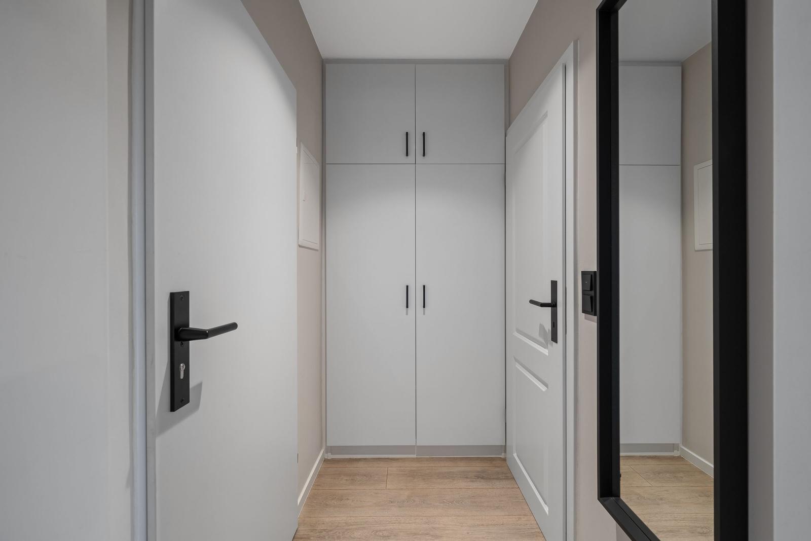Flur mit Schrank, Tür und Spiegel. Holzboden und neutrale Wandfarben.